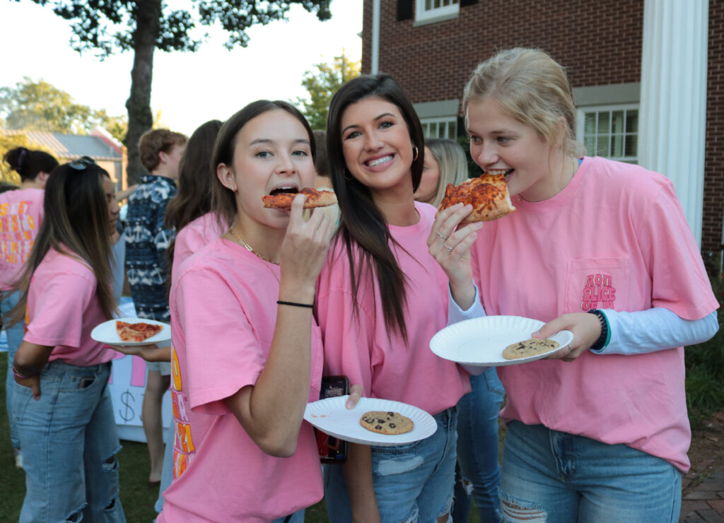 Photo of three girls eating pizza at a sorority fundraiser.